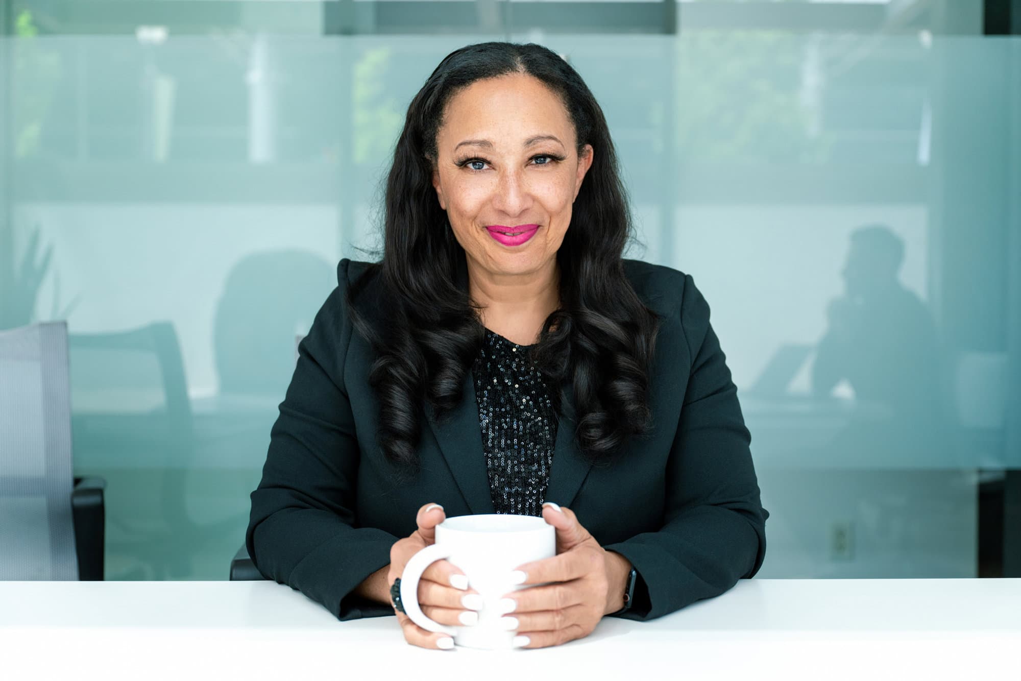 Dhorea Ramanula seated at a table, looking toward the camera with a warm, confident expression